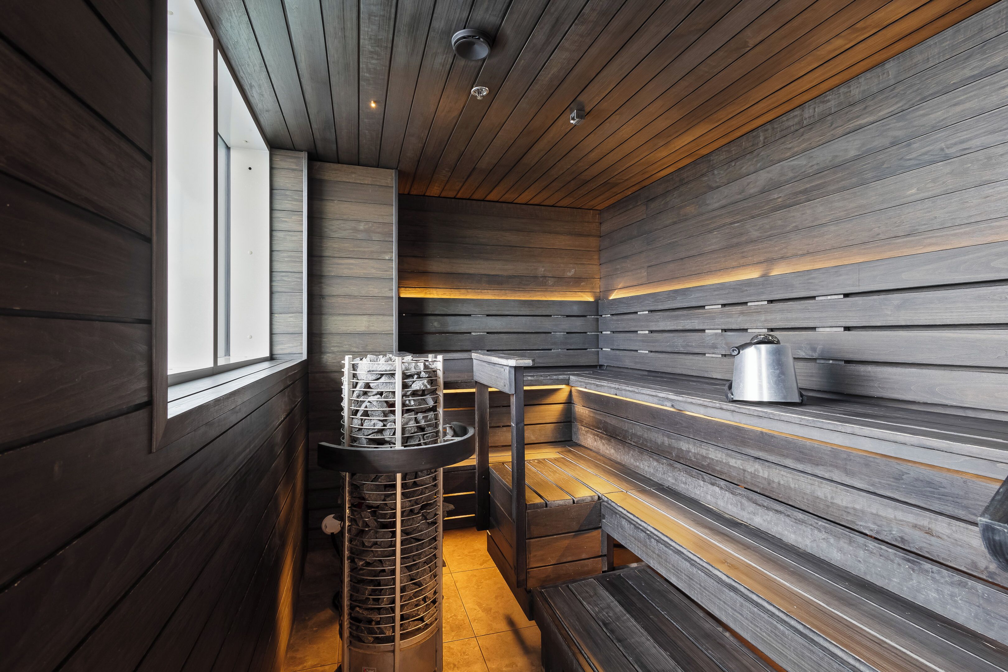 A sauna room with wooden walls, a bench, a heater, and a kettle on a shelf.