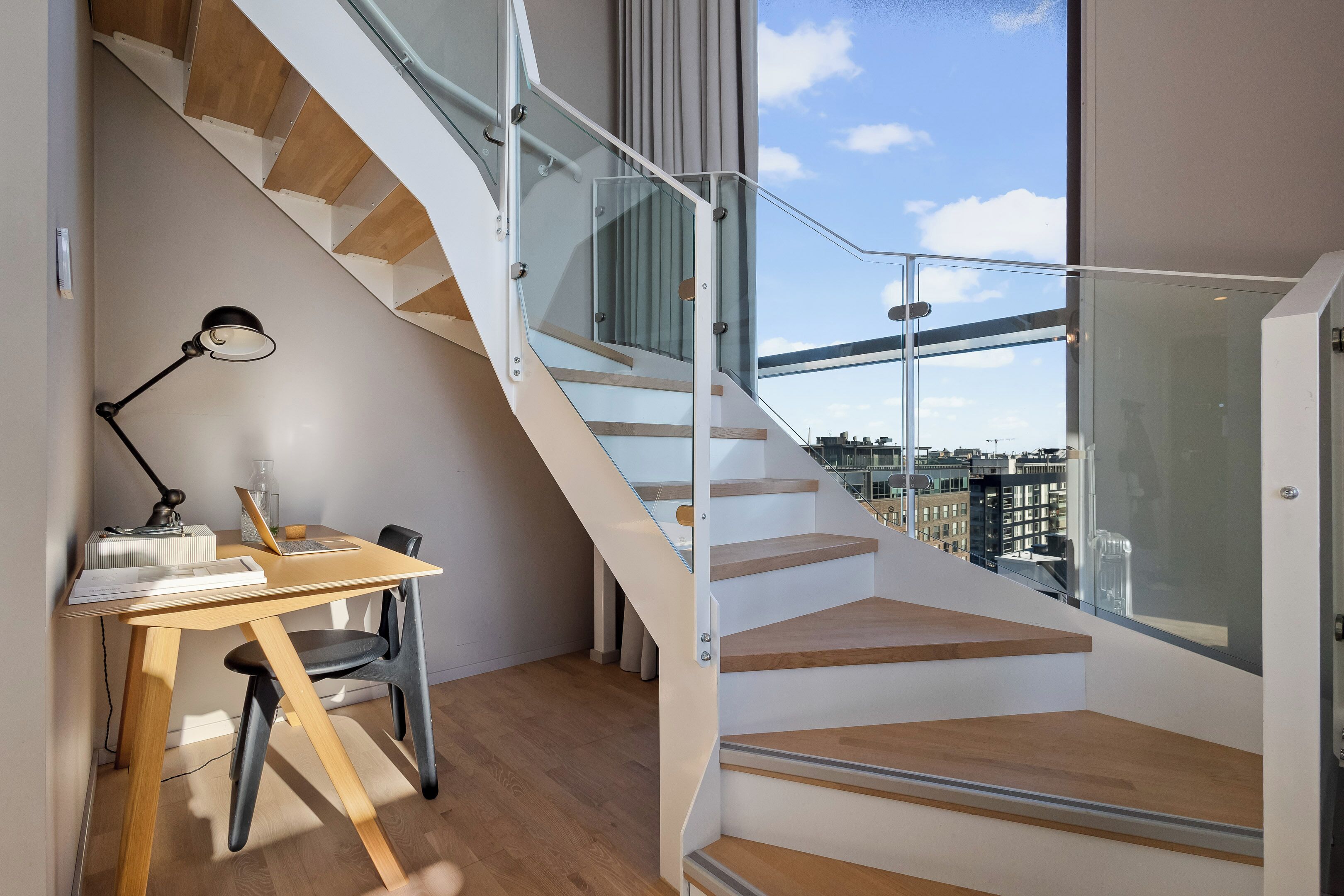 A modern interior with a wooden desk, chair, and a spiral staircase with glass railings.