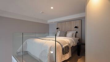 A modern bedroom with a glass partition, a bed with a white duvet, a bedside table, and a nightstand.