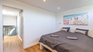 A bedroom with a bed, a painting of a beach scene, and a hallway leading to another room. - Beachhouse with garden and sauna just 700m from the beach (Schönberg)