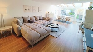 A modern living room with a large sectional sofa, a coffee table, and a dining area with chairs and a table. - Beachhouse with garden and sauna just 700m from the beach (Schönberg)