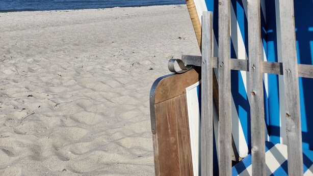 A beach chair with a blue and white striped cover and a woven edge, positioned on a sandy beach with a clear blue sky and calm sea in the background. - Beachhouse with garden and sauna just 700m from the beach (Schönberg)