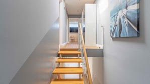 A modern staircase with wooden steps and a glass railing, leading to a room with a view of the sea. - Beachhouse with garden and sauna just 700m from the beach (Schönberg)