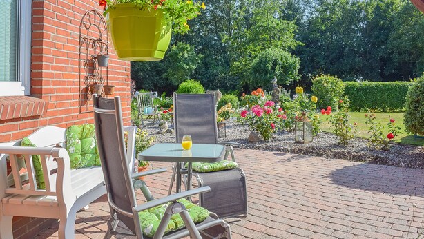Un patio al aire libre con un banco blanco, una mesa de vidrio y sillas con cojines verdes.