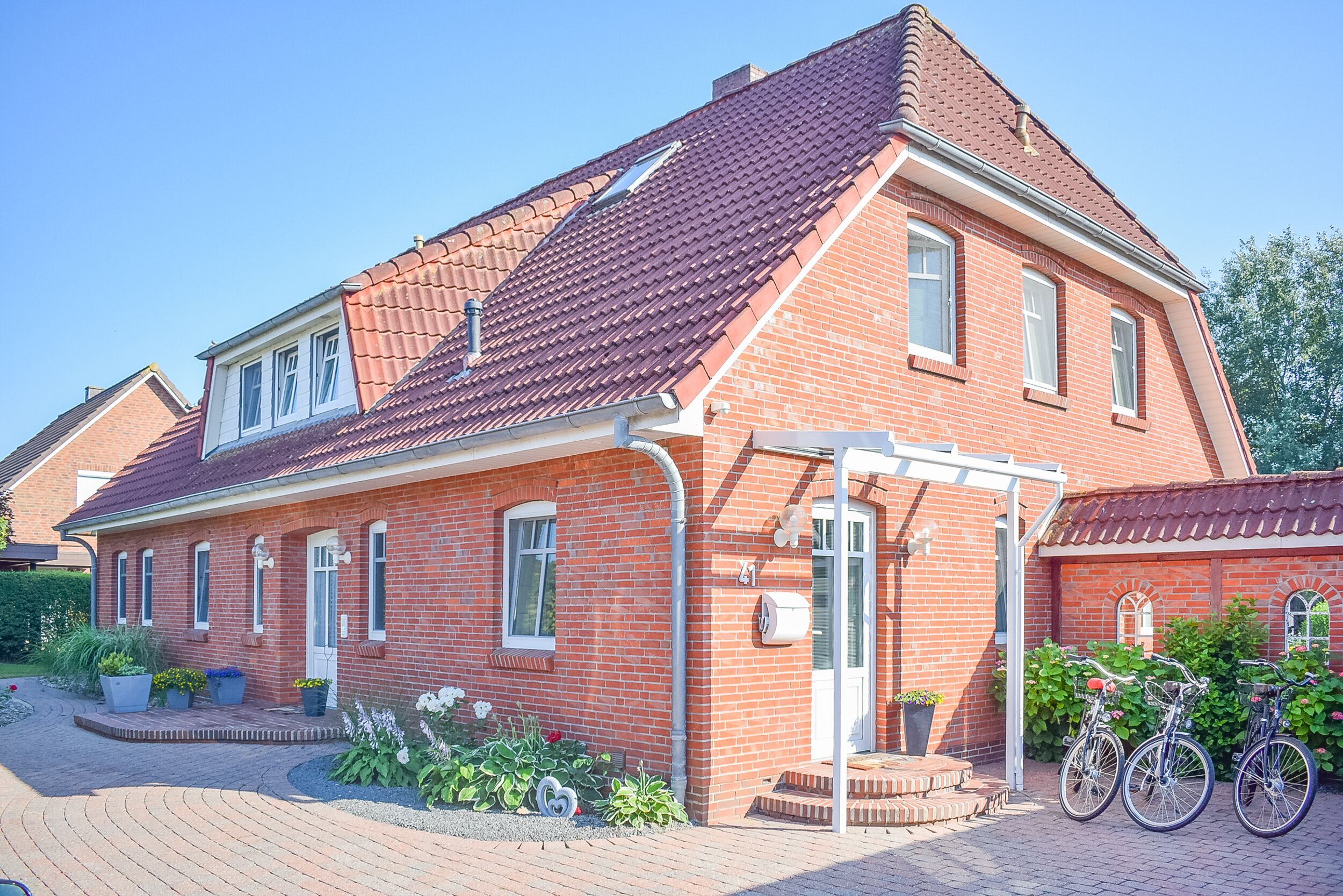 A red brick house with a tiled roof, a front porch, and a small garden with potted plants.