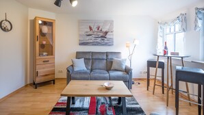 Una sala de estar con un sofá gris, un mueble de madera y un cuadro de un velero.