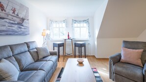 Una sala de estar con un sofá gris, una mesa de centro de madera, dos taburetes altos y un cuadro en la pared.