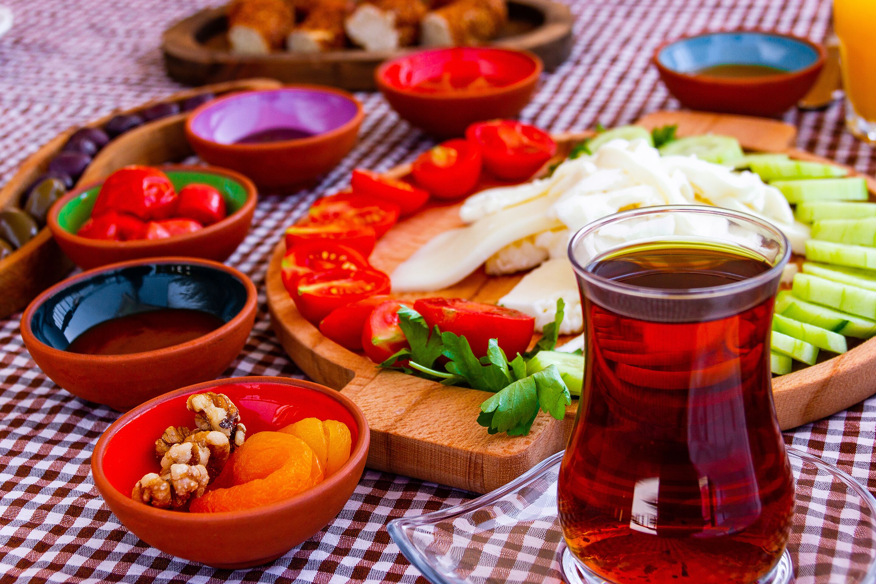 A table with various food items and a glass of red beverage, possibly tea, on a checkered tablecloth.