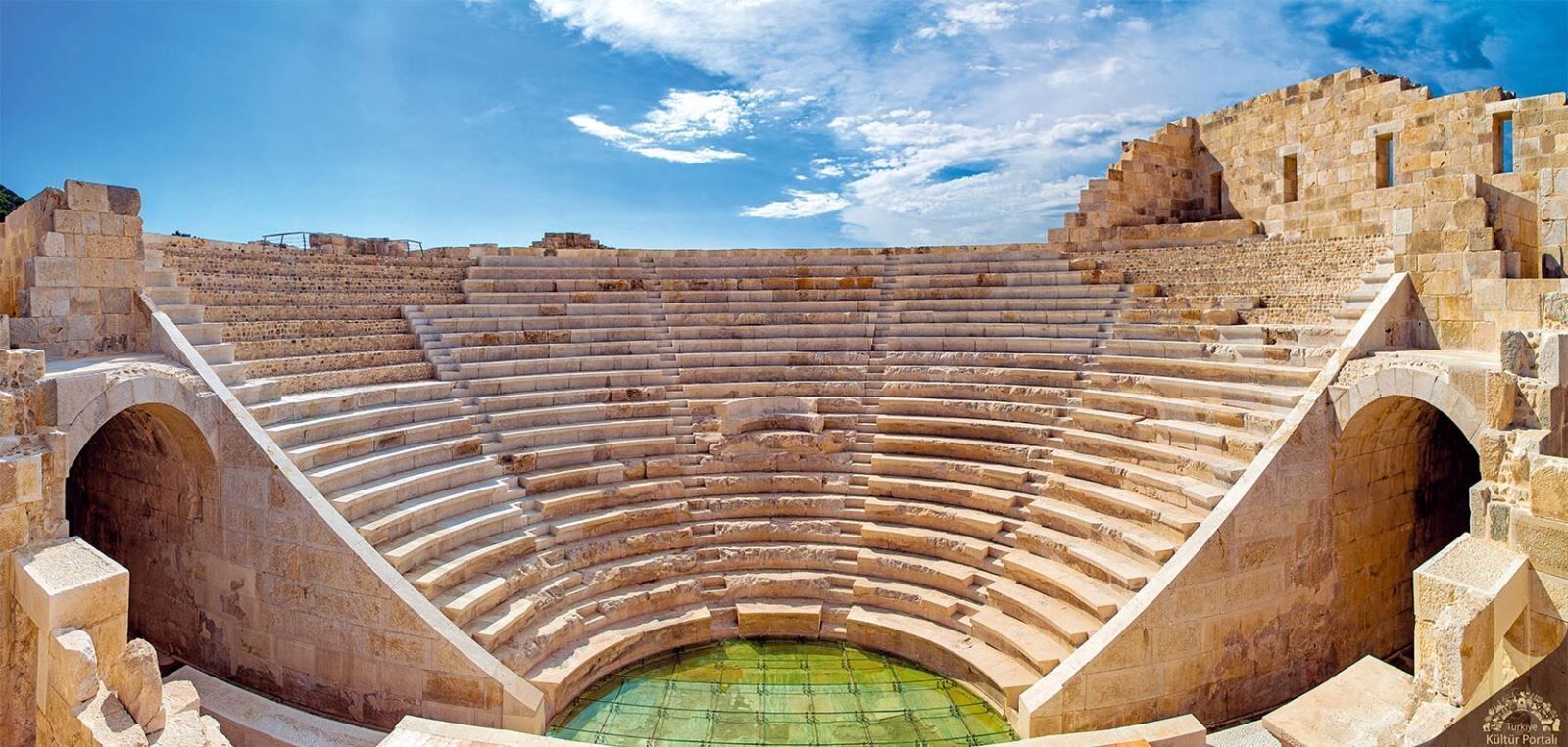 Un antiguo anfiteatro con asientos de piedra escalonados y un escenario central.