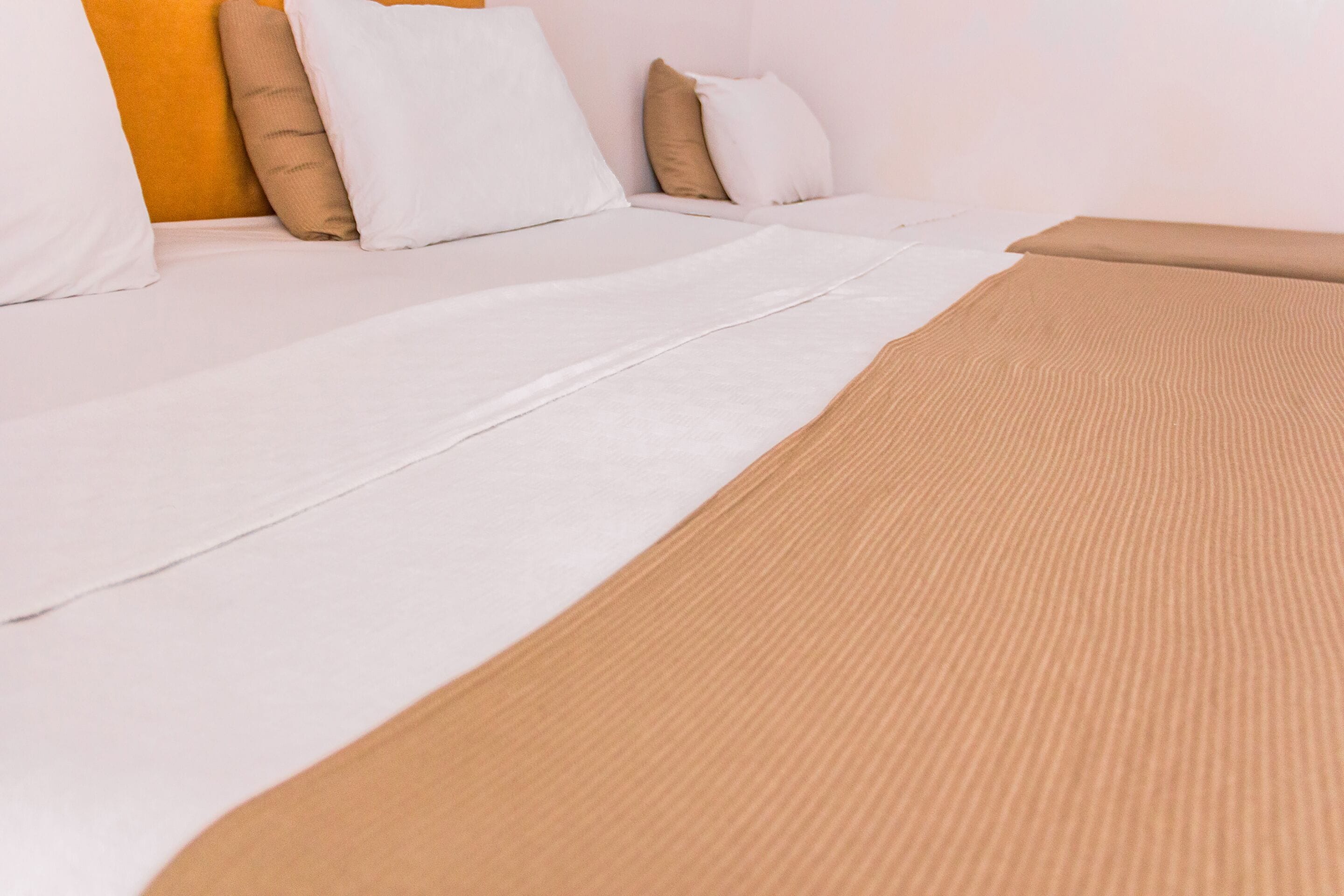 A bed with white and beige bedding, a brown textured blanket, and a white pillow.