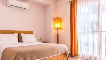 Una habitación de hotel con una cama, aire acondicionado, una lámpara y una ventana con cortinas.