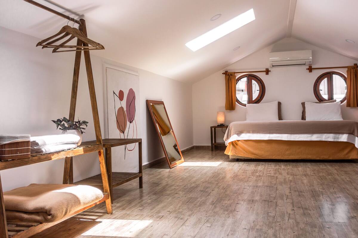 A bedroom with a bed, a wooden dresser, a mirror, and a window with curtains.