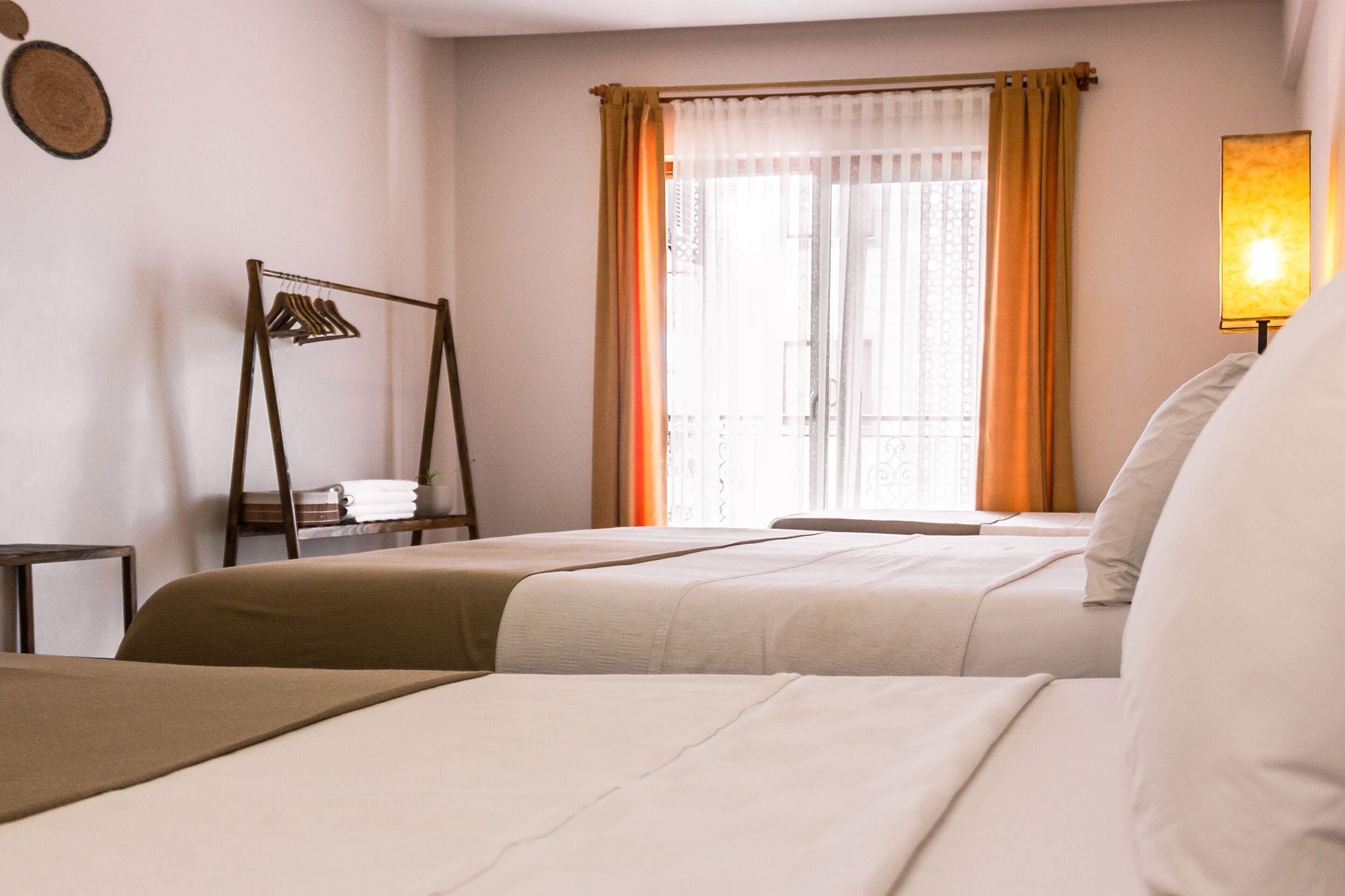 A hotel room with two beds, a window with curtains, a bedside table, and a lamp.