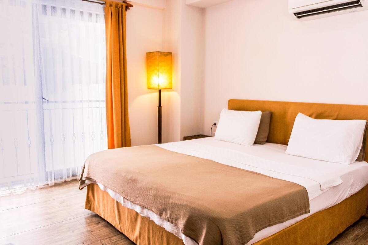 A hotel room with a bed, a nightstand, a lamp, and a window with curtains.