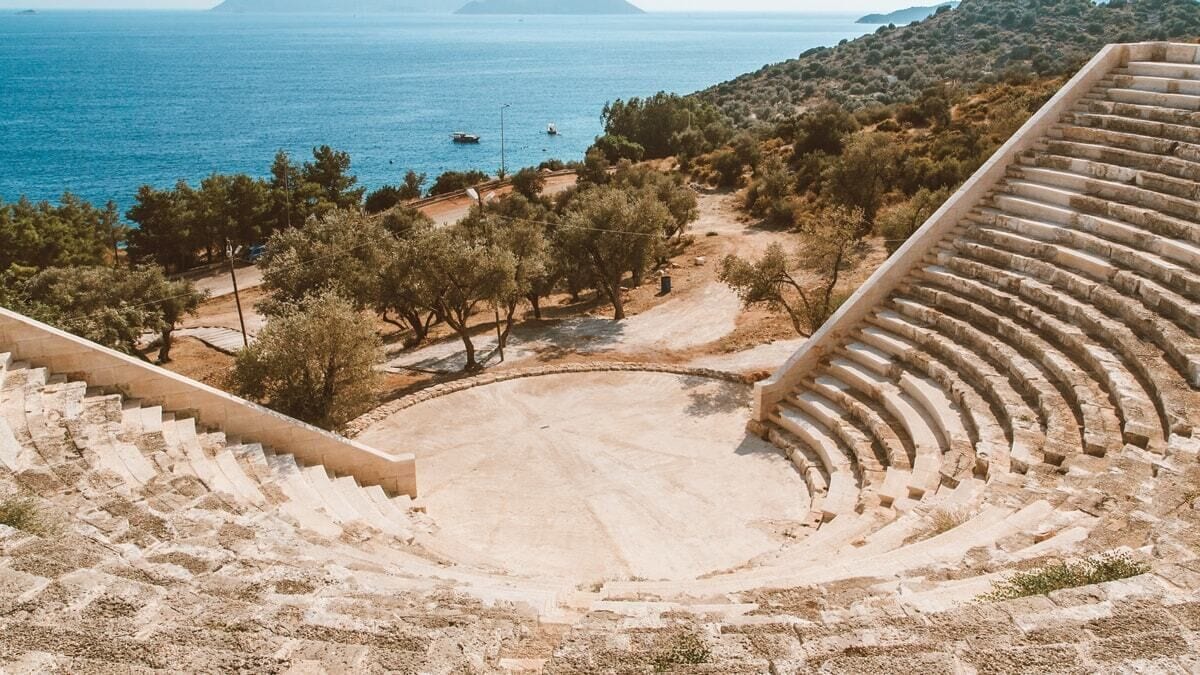An outdoor amphitheater with stone steps and a clear view of the sea and distant hills.