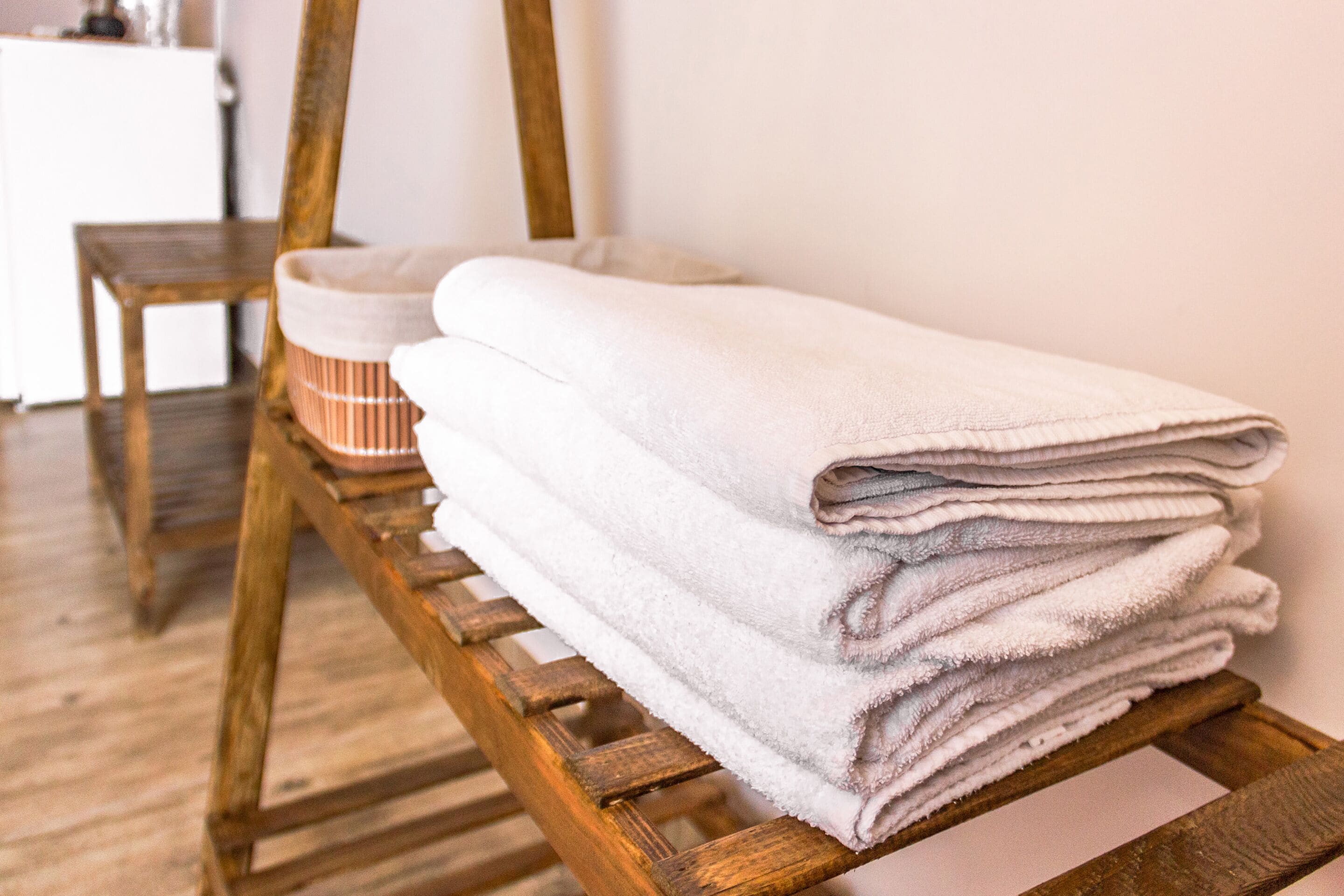 A stack of white towels on a wooden rack in a room with wooden flooring and a white wall.