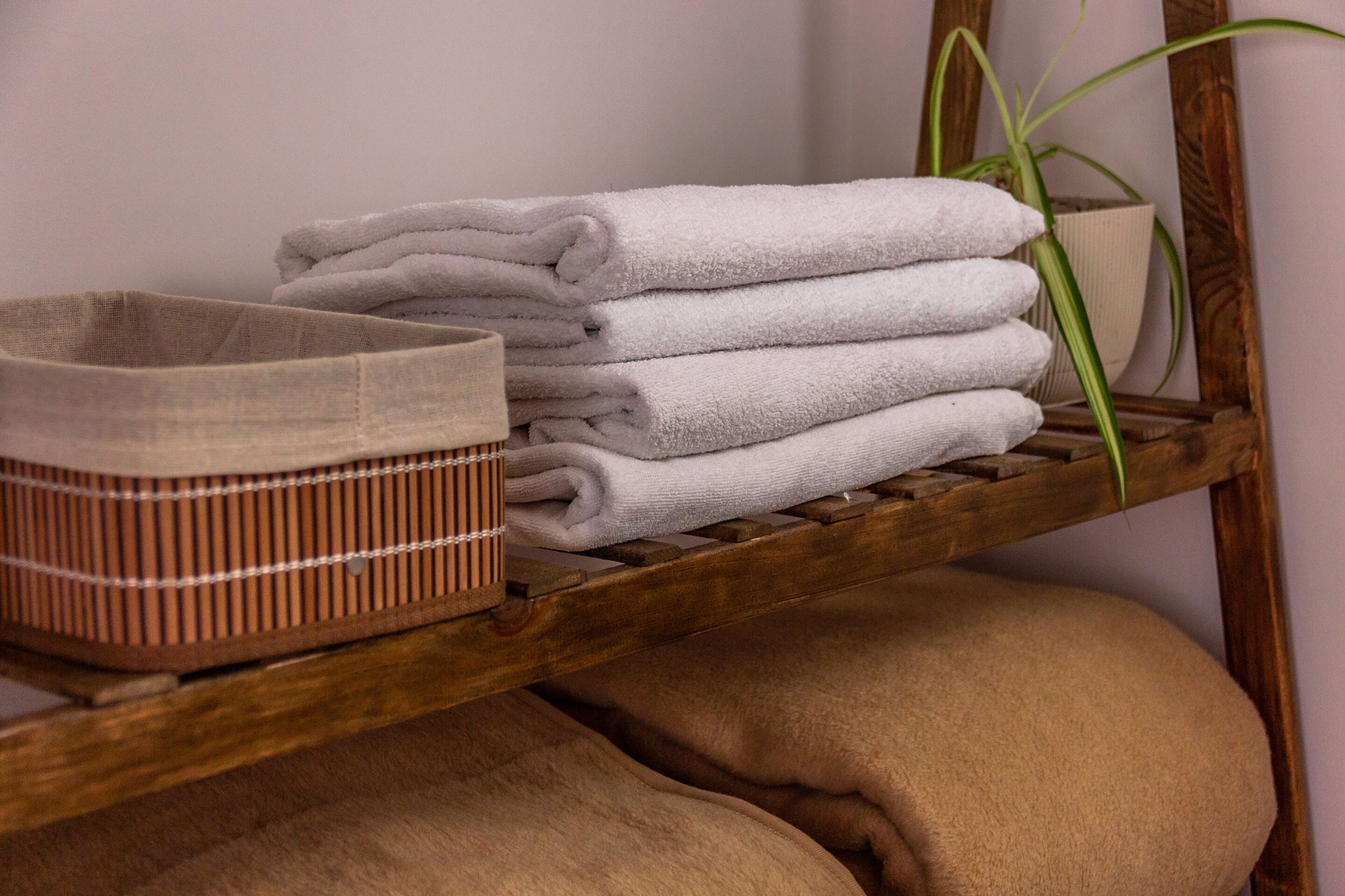 A shelf with neatly folded towels, a woven basket, and a potted plant.