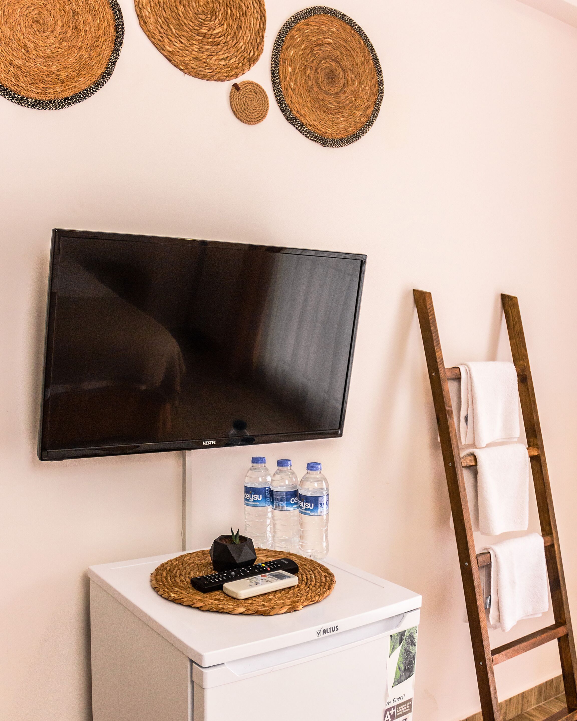 A room with a flat-screen TV mounted on the wall, a small white appliance, and a wooden ladder with towels.