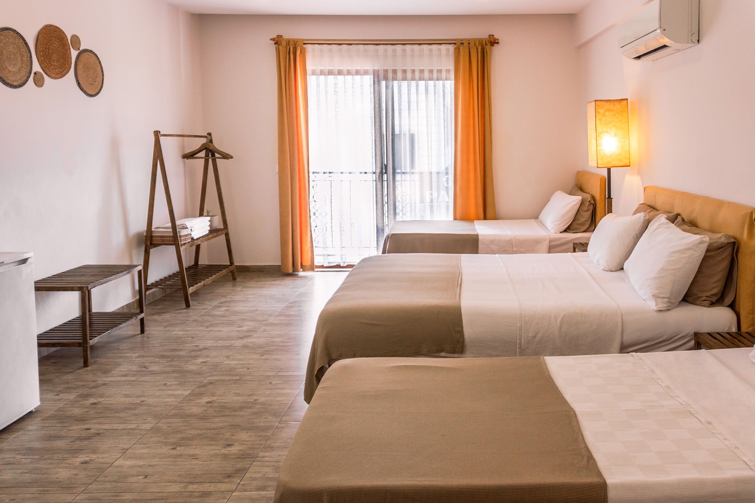A hotel room with two beds, a wooden shelf, a hanging rack, and a balcony with curtains.