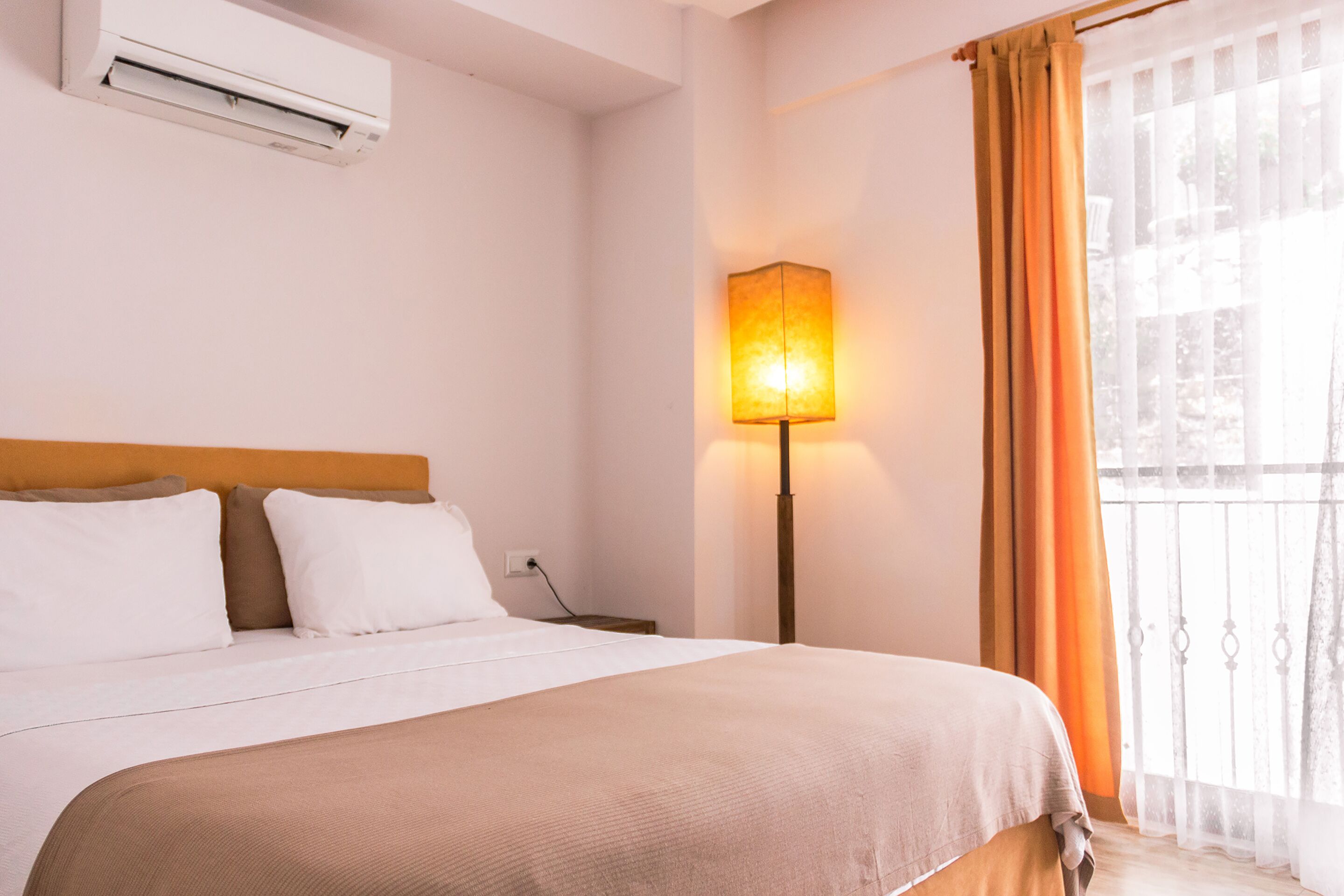 A hotel room with a bed, a bedside lamp, an air conditioner, and a window with curtains.