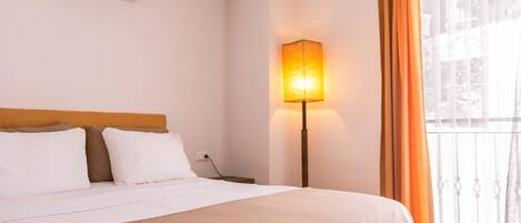 A hotel room with a bed, a bedside lamp, an air conditioner, and a window with curtains.