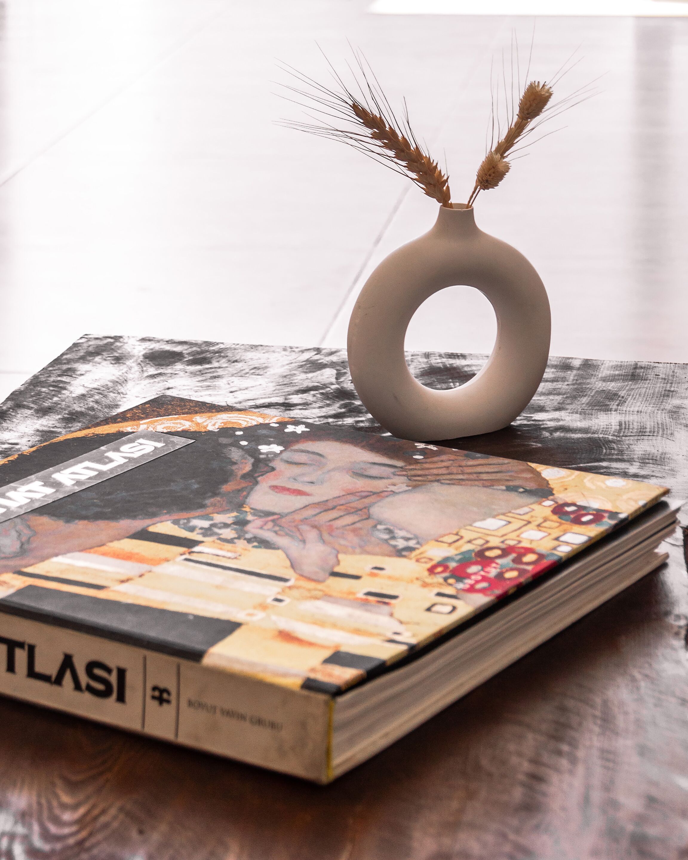 A book titled "TLASI" on a wooden surface with a vase containing wheat stalks.