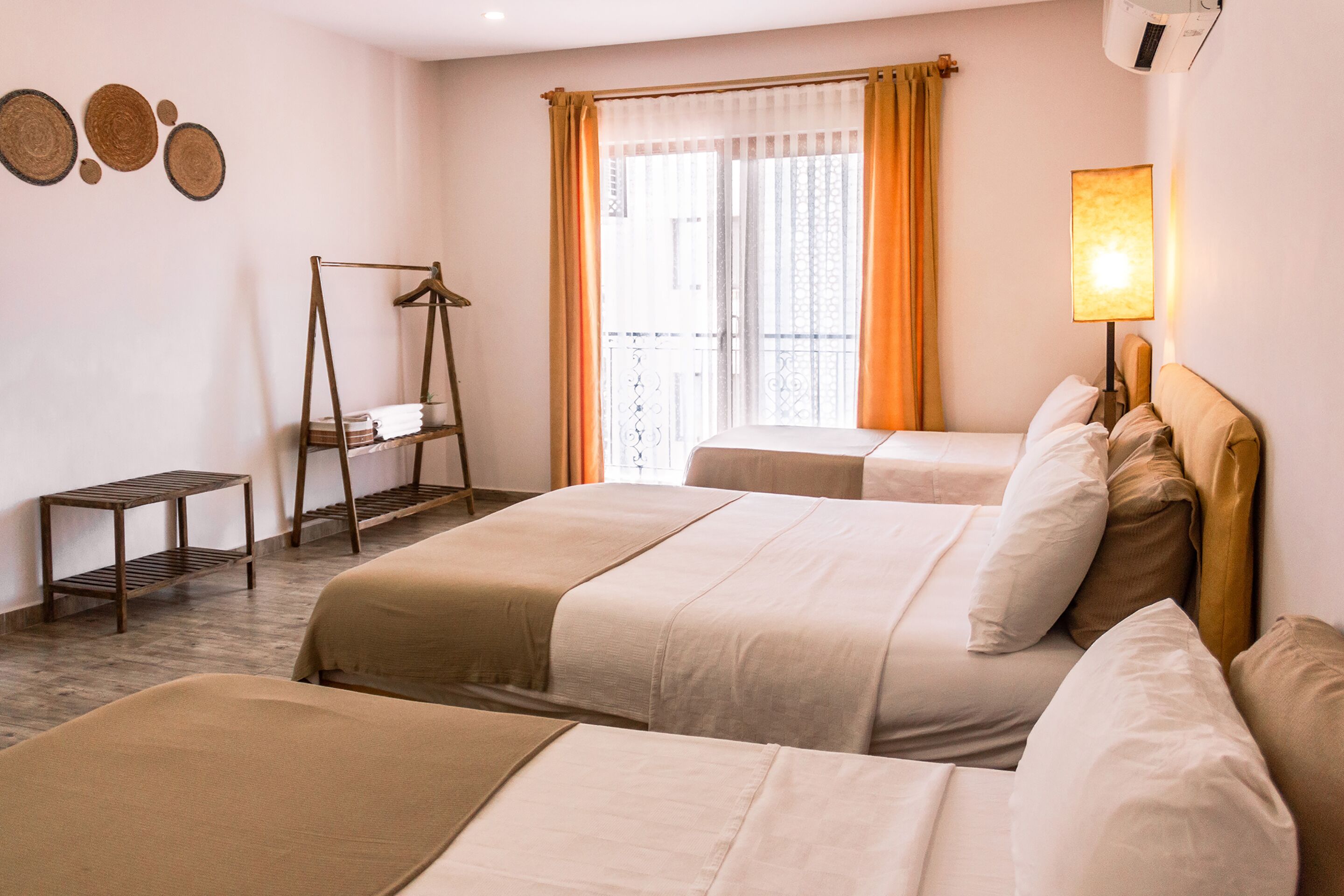 A hotel room with two beds, a small table, a hanging chair, and a window with curtains.