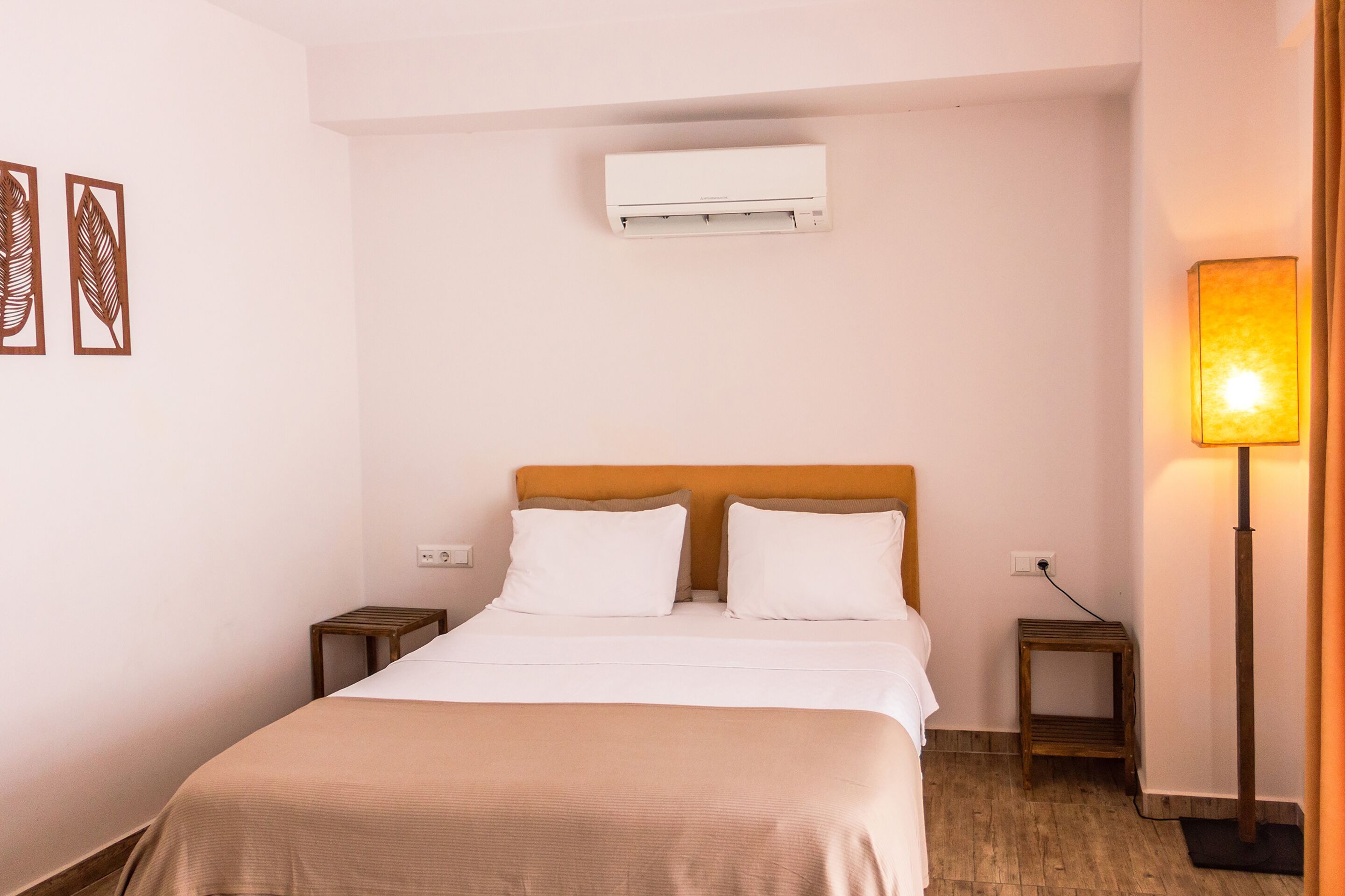 A neatly arranged hotel room with a bed, bedside tables, an air conditioner, a lamp, and artwork on the wall.