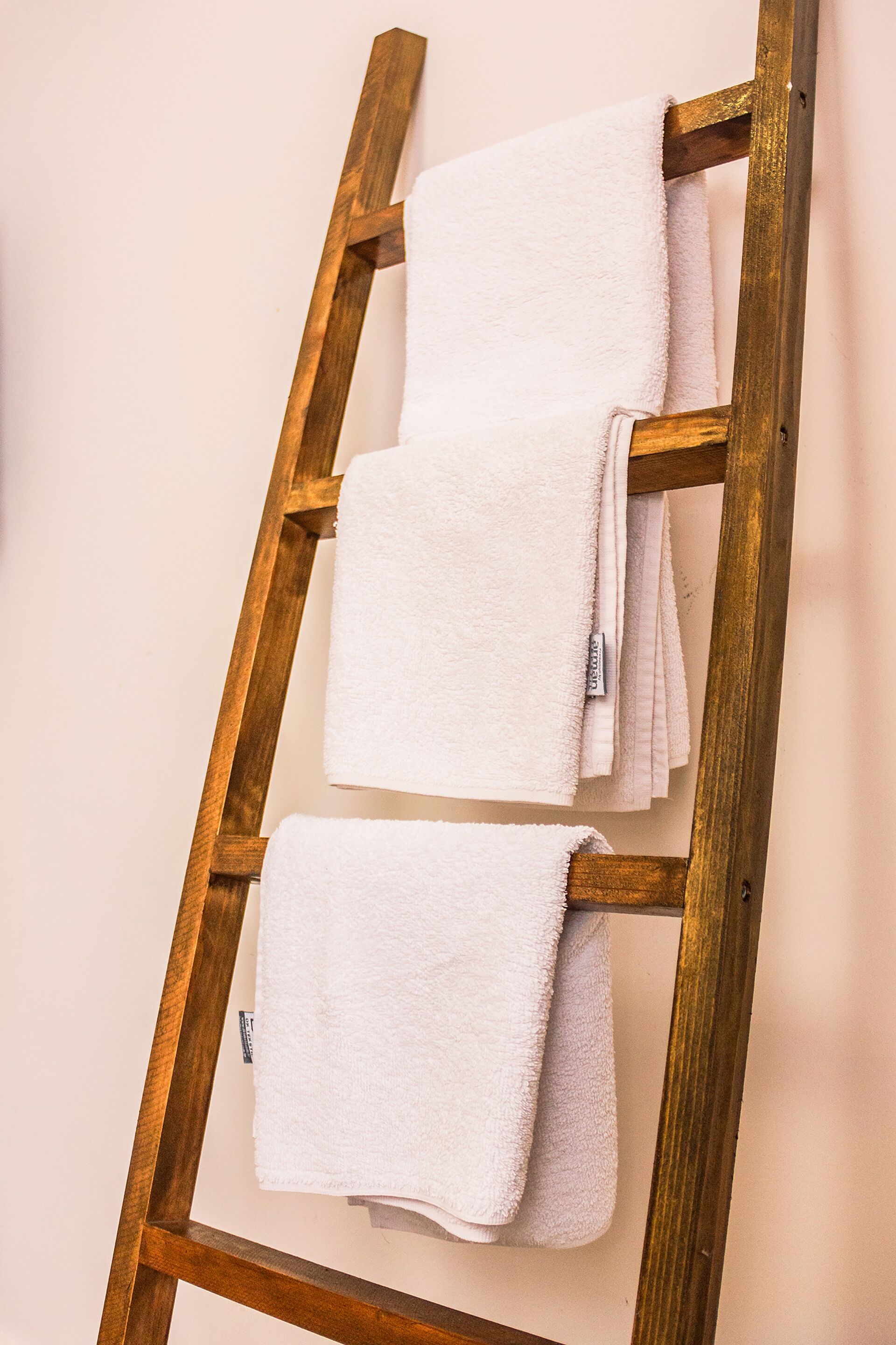 Une échelle en bois sur laquelle sont suspendues trois serviettes blanches.