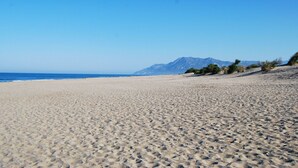 Een uitgestrekt zandstrand met een heldere lucht en bergen in de verte.