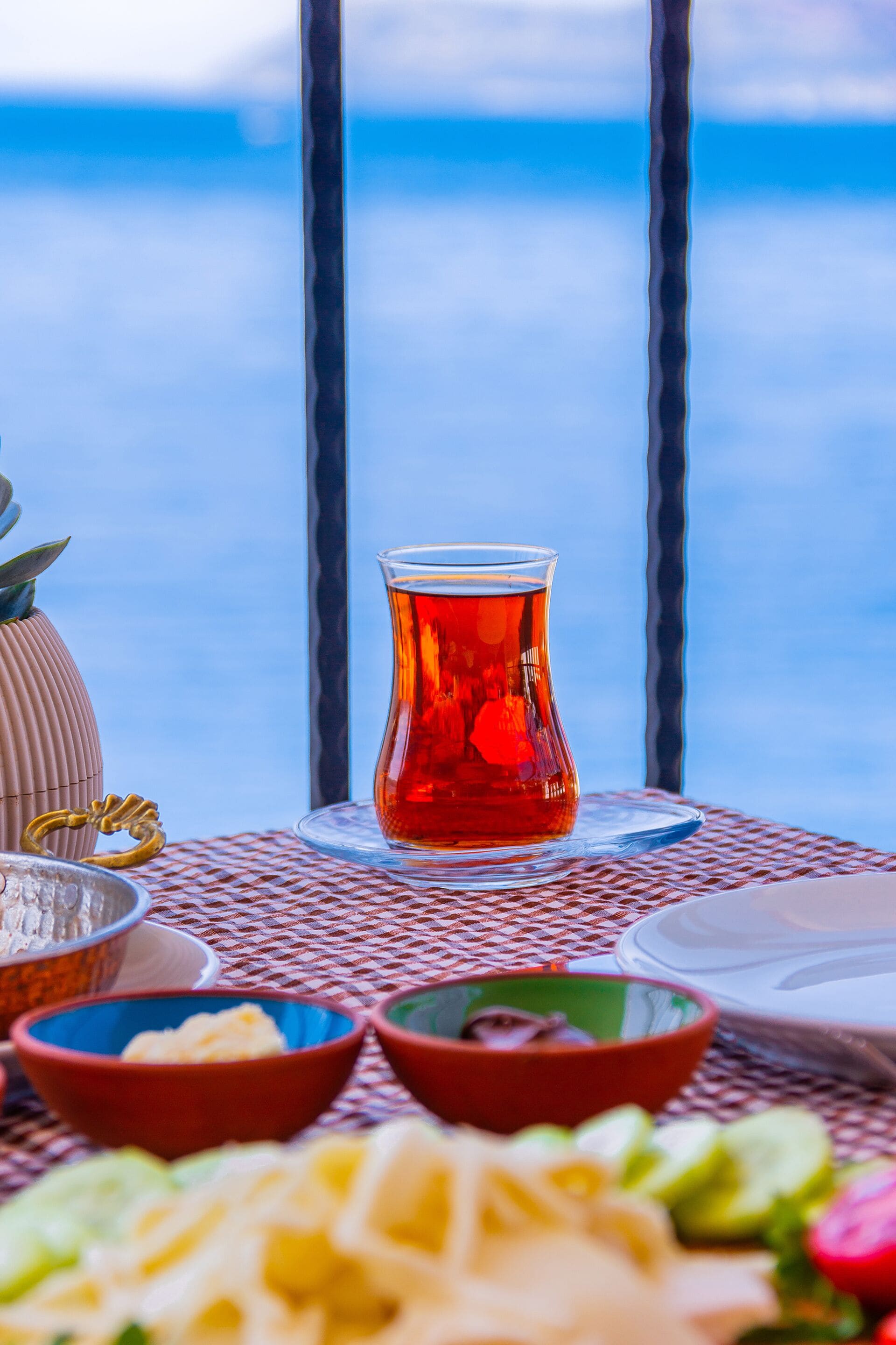 A table set with a glass of tea, bowls of food, and a view of the sea.