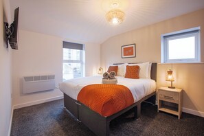 A bedroom with a bed, bedside table, lamp, and a window.