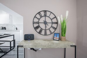 Una cocina moderna con un reloj de pared grande, una mesita con un marco de fotos y una planta, y un altavoz sobre la encimera.