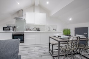 A modern kitchen with white cabinetry, a built-in oven, and a dining area with a table and chairs.