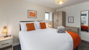 Moderni hotellihuone, jossa on suuri sänky, puinen vaatekaappi, yöpöytä lampulla ja ikkuna, josta on näkymä.