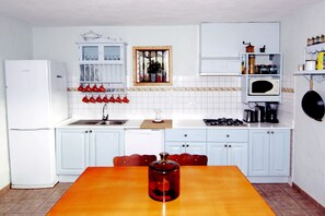 A kitchen with white cabinets, a wooden table, a red vase, and a microwave.
