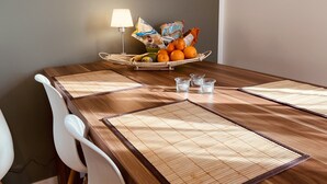 Un tavolo da pranzo in legno con un sottopiattino intrecciato, un cesto d'arance e una lampada sullo sfondo.
