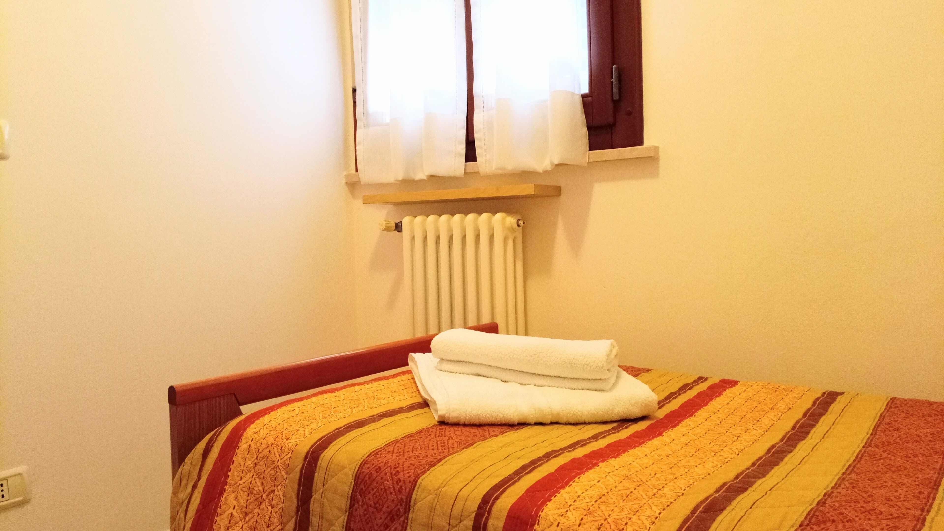 Une chambre à coucher avec un lit, une fenêtre avec des rideaux, un radiateur et une prise électrique.