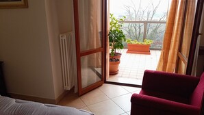 A room with a sliding glass door leading to a balcony with potted plants. - Apartment with beautiful view of the hills, between Pesaro and Fano (Mombaroccio)