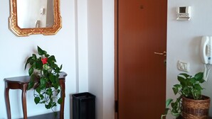 A room with a wooden door, a mirror with a gold frame, a small table with a potted plant, and a trash bin. - Apartment with beautiful view of the hills, between Pesaro and Fano (Mombaroccio)
