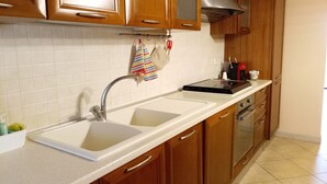 A kitchen with wooden cabinets, a stainless steel sink, and a black stove. - Apartment with beautiful view of the hills, between Pesaro and Fano (Mombaroccio)