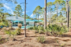Una casa moderna con piscina, rodeada de pinos y plantas tropicales.