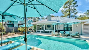 A swimming pool with lounge chairs and umbrellas, a covered patio area, and a house with a metal roof and large windows. - Wood Beach Retreat – Perfect 30A Location offering Easy Beach Access & Private Pool (Santa Rosa Beach)