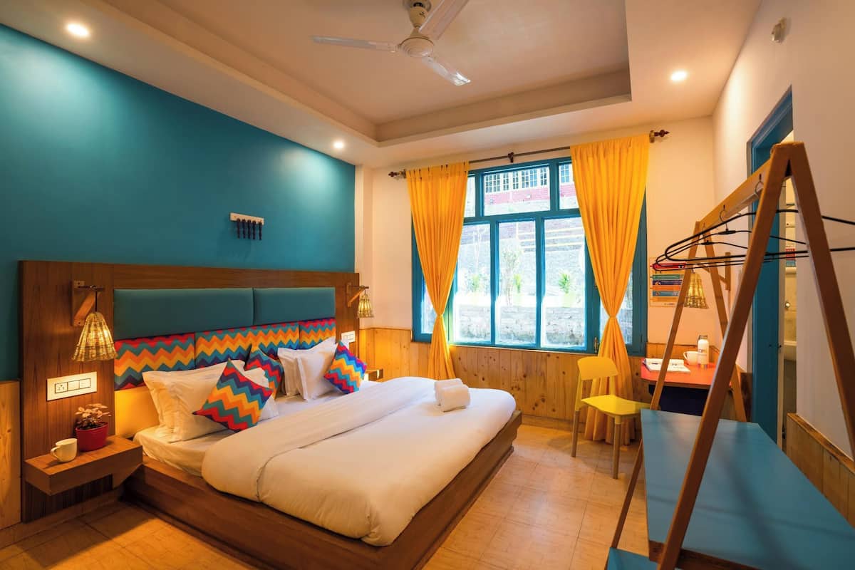 A bedroom with a bed, bedside table, lamp, window with curtains, and a desk with chair.