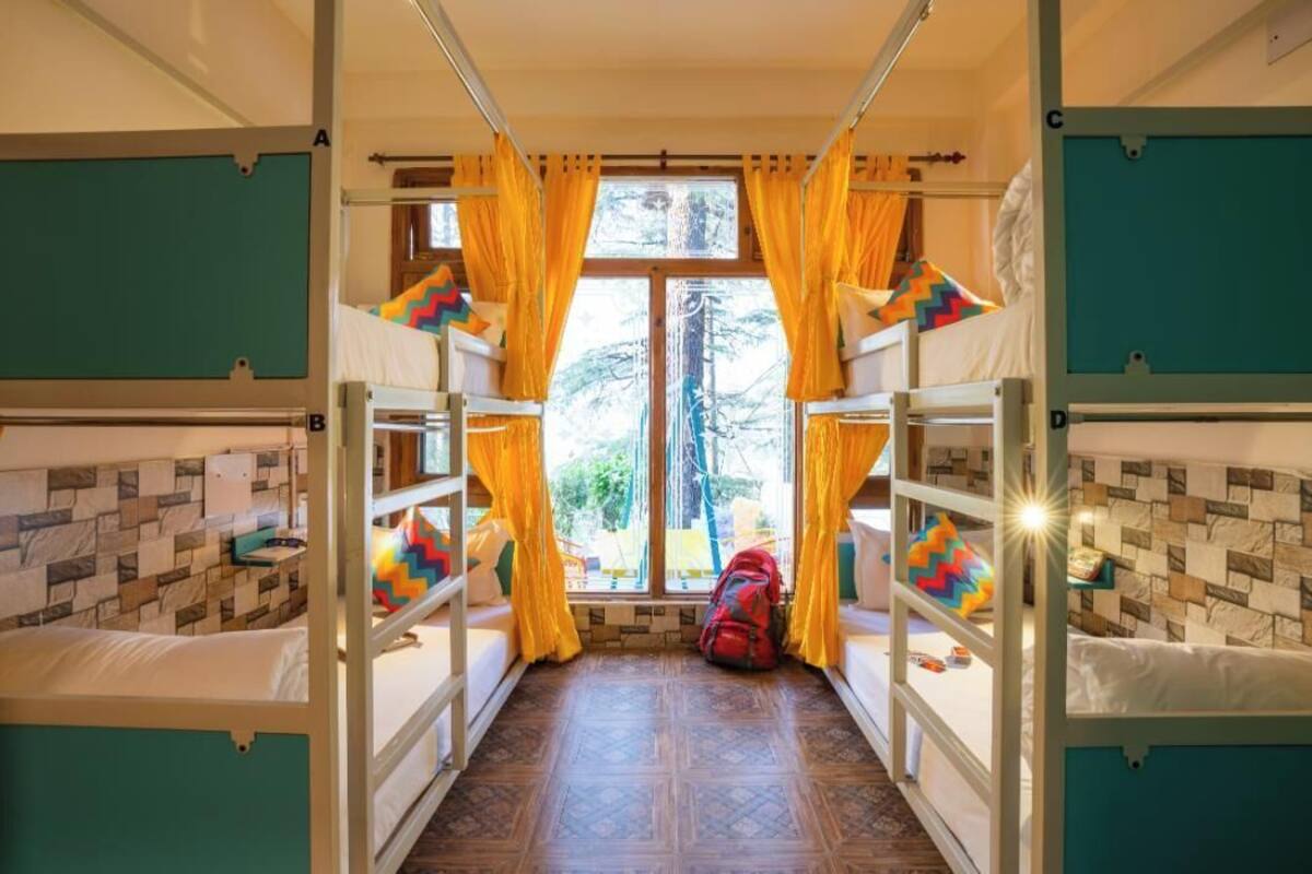 A dormitory room with bunk beds, a window with curtains, and a backpack on the floor.