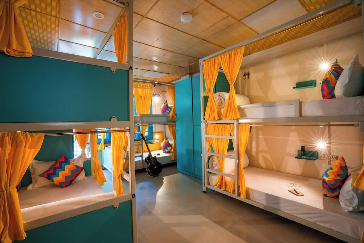 A room with bunk beds, each with orange curtains, and a guitar on one bed.