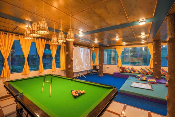 A pool table with balls, a projector screen, and a seating area with cushions. - goSTOPS Kasol (Bhuntar)