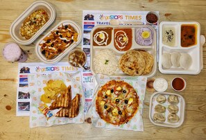 Une variété de plats, notamment des nachos, du riz, du pain pita, des pizzas et des raviolis, disposés sur une table en bois.