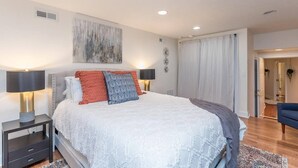 Un dormitorio moderno con una cama grande, dos lámparas de noche, un elemento decorativo en la pared y vistas al pasillo.