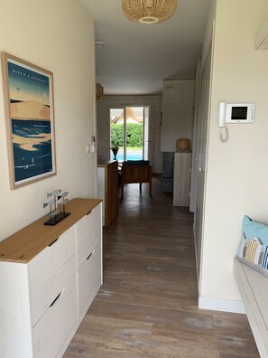 A modern kitchen with wooden cabinets, a dining area with a table and chairs, and a view of a swimming pool through an open door.